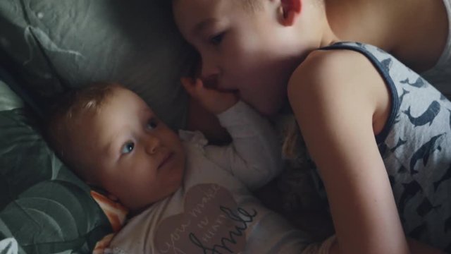 Medium shot of an older brother playing with baby sister while in bed at home. Filmed in low-key.