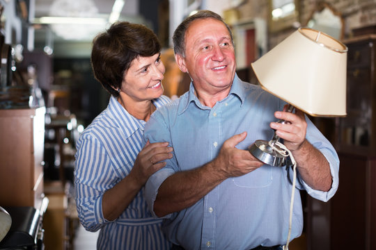 satisfied mature couple is shopping the old lamp in the antique store