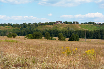 Landscape view of the village located on a hilly area. A field with dry herbs. Summer beautiful day.