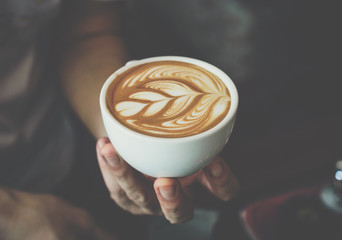 Close up of Barista holding a cup of coffee with latte art.