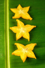 Slices of ripe yellow star fruit carambola or star apple ( starfruit ) on green banana leaf, vertical composition © 18042011