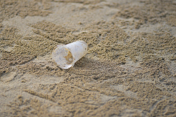 Plastic glass is on the beach, Trash on sand beach showing environmental pollution problem. Concept is the human is the main cause of world environmental problem.