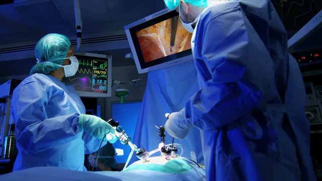 Laparoscopy Medical training operation transmitted on hospital monitors performed by Caucasian hospital surgeons wearing gloves and scrubs 