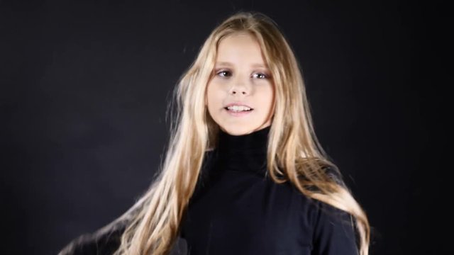 Portrait of a cute white-skinned teenaged girl little model isolated on black posing. 4k
