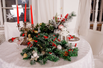 Fototapeta na wymiar Christmas Family Dinner Table Concept.Table setting for new year dinner.decorations, candles and lanterns. white tablecloth. Living room decorated with lights and Christmas tree. Holiday setting