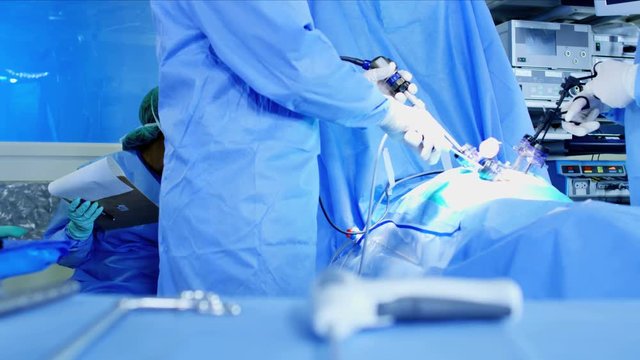 Laparoscopy surgical operation transmitted on hospital video monitors being performed by Caucasian surgeons using an Endoscopy and surgical tools while wearing protective clothing 