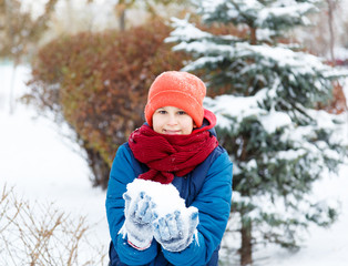 cute young boy in red hat blue jacket holds and plays with snow, has fun, smiles, makes snowman in winter park. Active lifestyle, winter activity, outdoor winter games, snowballs. 