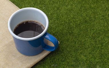 Coffee in blue tin cup on grass background.