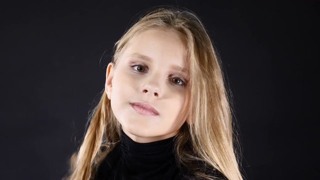 Pretty little model posing in studio isolated on black. White - haired girl looks at camera, smiling, 4k