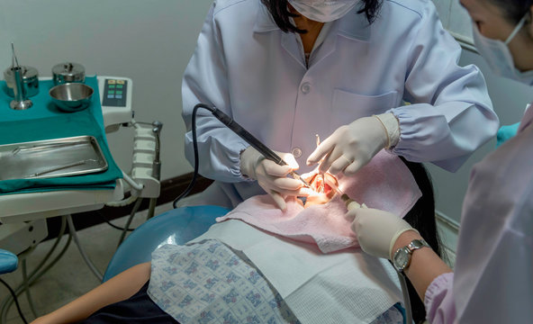 Close up fo Asian dentist examines young girl patient using mirror for teeth checkup and cleaning her teeth of tartar and plaque.