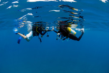 Fototapeta na wymiar Young Asian couple scuber diver in love holding hands and taking picture in clear blue waters at surface , Koh Chang Island, the tourist attraction in gulf of Thailand.