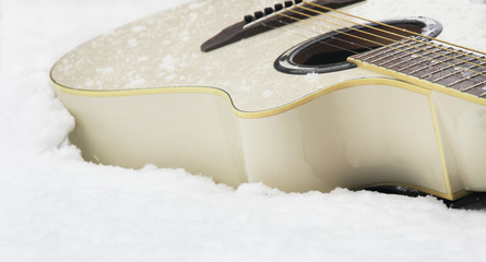 Milk white colour acoustic wooden guitar laying on the whine snow. Beautiful guitar close view in...
