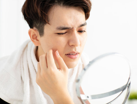 young man looking to mirror and squeezing pimple