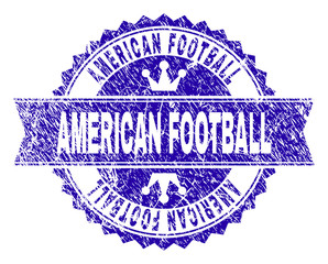 AMERICAN FOOTBALL rosette seal imitation with grunge texture. Designed with round rosette, ribbon and small crowns. Blue vector rubber print of AMERICAN FOOTBALL title with grunge texture.