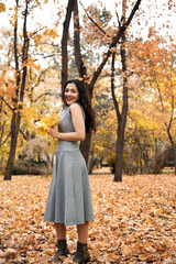 Pretty woman posing with maple's leaf in autumn park near big tree. Beautiful landscape at fall season.