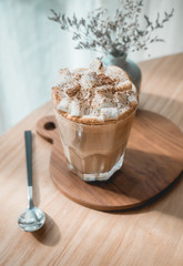 One glass of hot coffee with marshmallow on top serve on white tray on wood table next to bright window in morning.