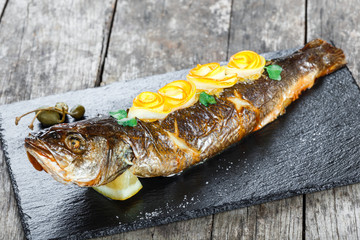 Grilled sea fish with lemon on stone slate background close up. Healthy food. Top view