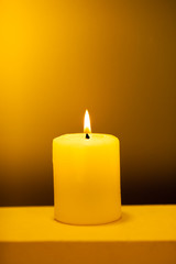 Large lighted candle on a warm yellow background.