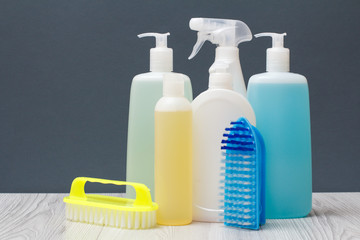 Bottles of detergent and brushes for cleaning on gray background.