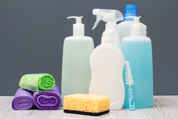 Bottles of detergent, garbage bags and sponge on gray background.