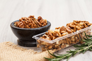 Walnuts in stone bowl and plastic container on a wooden background.
