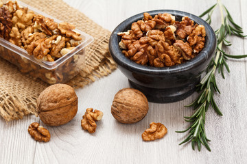 Walnuts in stone bowl and plastic container on a wooden background.