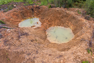 Holes on ground from powerful explosions. Bomb craters in the forest. Disposal of explosives. Top view aerial photo from flying drone.