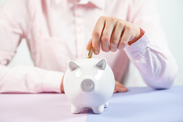 Hand putting coin into piggy bank closeup. Selective focus.