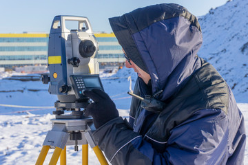A surveyor conducts a topographical survey for the cadastre at a construction site in winter