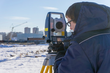 A surveyor conducts a topographical survey for the cadastre at a construction site in winter