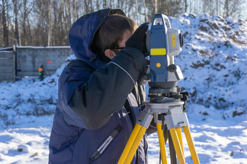 Fototapeta na wymiar A surveyor with an assistant makes a topographical survey for the cadastre at a construction site in winter