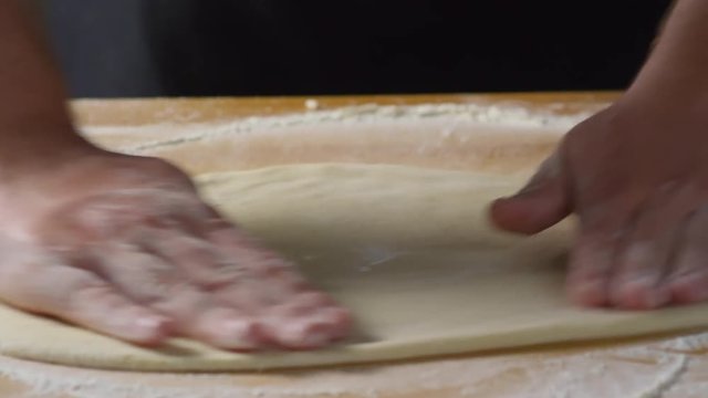Close up shot of hands of male cook stretching pizza dough on table