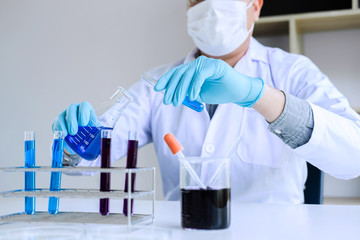 Biochemistry laboratory research, Scientist or medical in lab coat holding test tube with reagent with drop of color liquid over glass equipment working at the laboratory