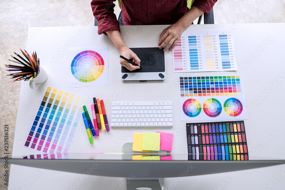 Poster Image of female creative graphic designer working on color selection and drawing on graphics tablet at workplace, top view workspace