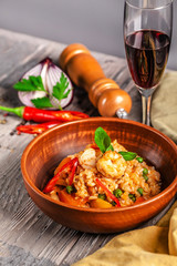 Concept of Spanish cuisine. Paella with seafood and shrimps, with green peas in a clay plate. A glass of cool wine is on the table.