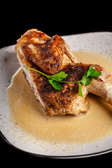 The concept of Georgian cuisine. Half a baked chicken in garlic sauce with crispy crust on a white plate, on a black background.