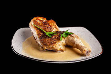 The concept of Georgian cuisine. Half a baked chicken in garlic sauce with crispy crust on a white plate, on a black background.