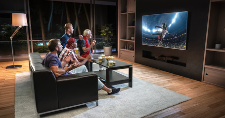 Group of fans are watching a soccer moment on the TV and celebrating a goal, sitting on the couch in the living room.