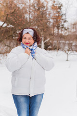 Fototapeta na wymiar Holidays days, Christmas winter time. Plus size Woman in coat and headband outdoor. Lady in casual clothes, plump lady fashion concept, posing on the street in snowy weather 