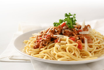 spaghetti plate with sauce from minced meat and tomato, parmesan and parsley garnish on a white table with copy space