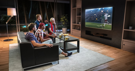 Group of fans are watching a soccer moment on the TV and celebrating a goal, sitting on the couch in the living room.
