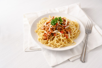 spaghetti with minced meat tomato sauce, parmesan and parsley garnish on a white table with copy space
