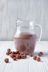 Healthy natural chocolate milk in glass jug with hazelnuts for breakfast