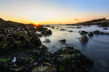 magical and orange sunset on a rocky beach in Porto, Portugal, Europe. Long exposure shot