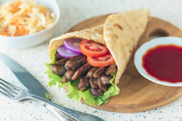 Handmade doner kebab is lying on the white table made of artificial stone Shawarma on the wooden cutting board with chicken meat, onions, salad lies on a dark old wooden table.