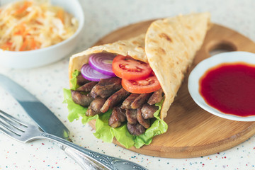 Handmade doner kebab is lying on the white table made of artificial stone Shawarma on the wooden cutting board with chicken meat, onions, salad lies on a dark old wooden table.