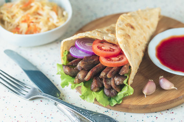 Handmade doner kebab is lying on the white table made of artificial stone Shawarma on the wooden cutting board with chicken meat, onions, salad lies on a dark old wooden table.