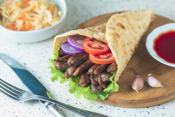Handmade doner kebab is lying on the white table made of artificial stone Shawarma on the wooden cutting board with chicken meat, onions, salad lies on a dark old wooden table.