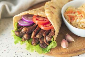 Handmade doner kebab is lying on the white table made of artificial stone Shawarma on the wooden cutting board with chicken meat, onions, salad lies on a dark old wooden table.