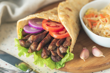 Handmade doner kebab is lying on the white table made of artificial stone Shawarma on the wooden cutting board with chicken meat, onions, salad lies on a dark old wooden table.
